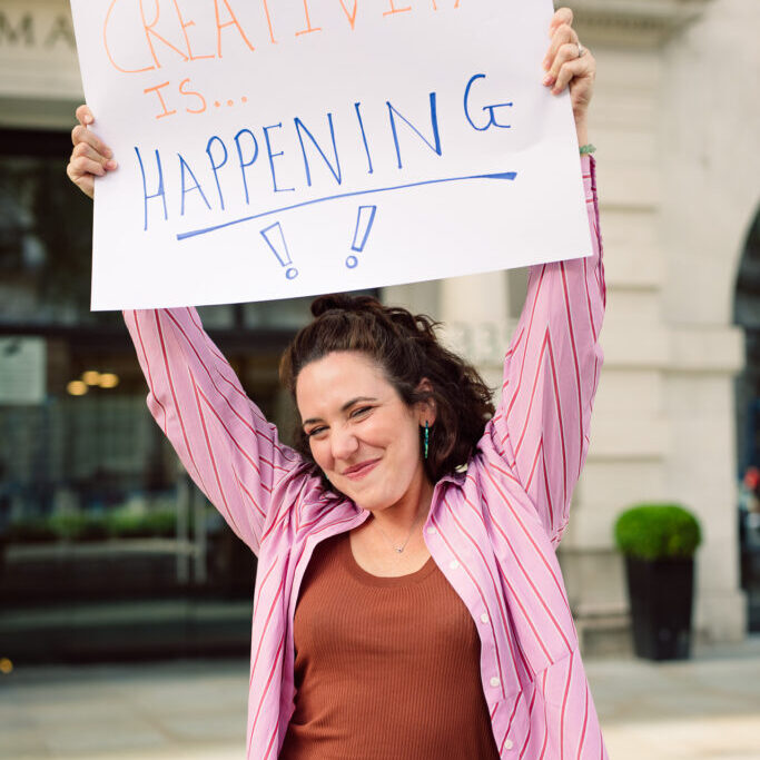 Jemima holding up a sign that says "Creativity is Happening"