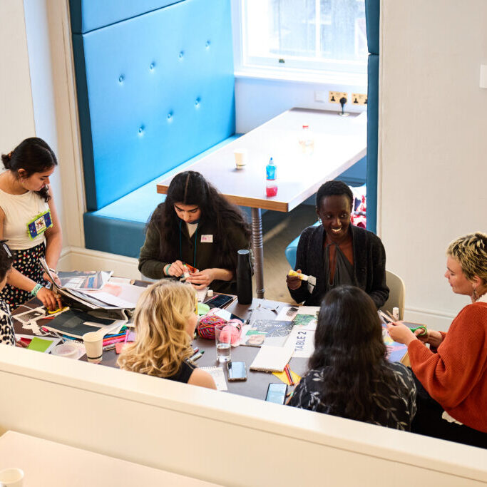 A group of young people sat around a table, creating and in conversation.